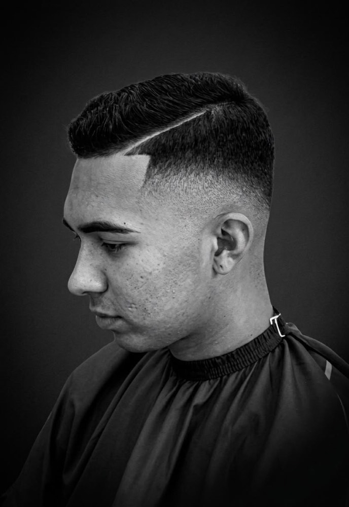 Skin fade con raya marcada al costado, degradado a piel